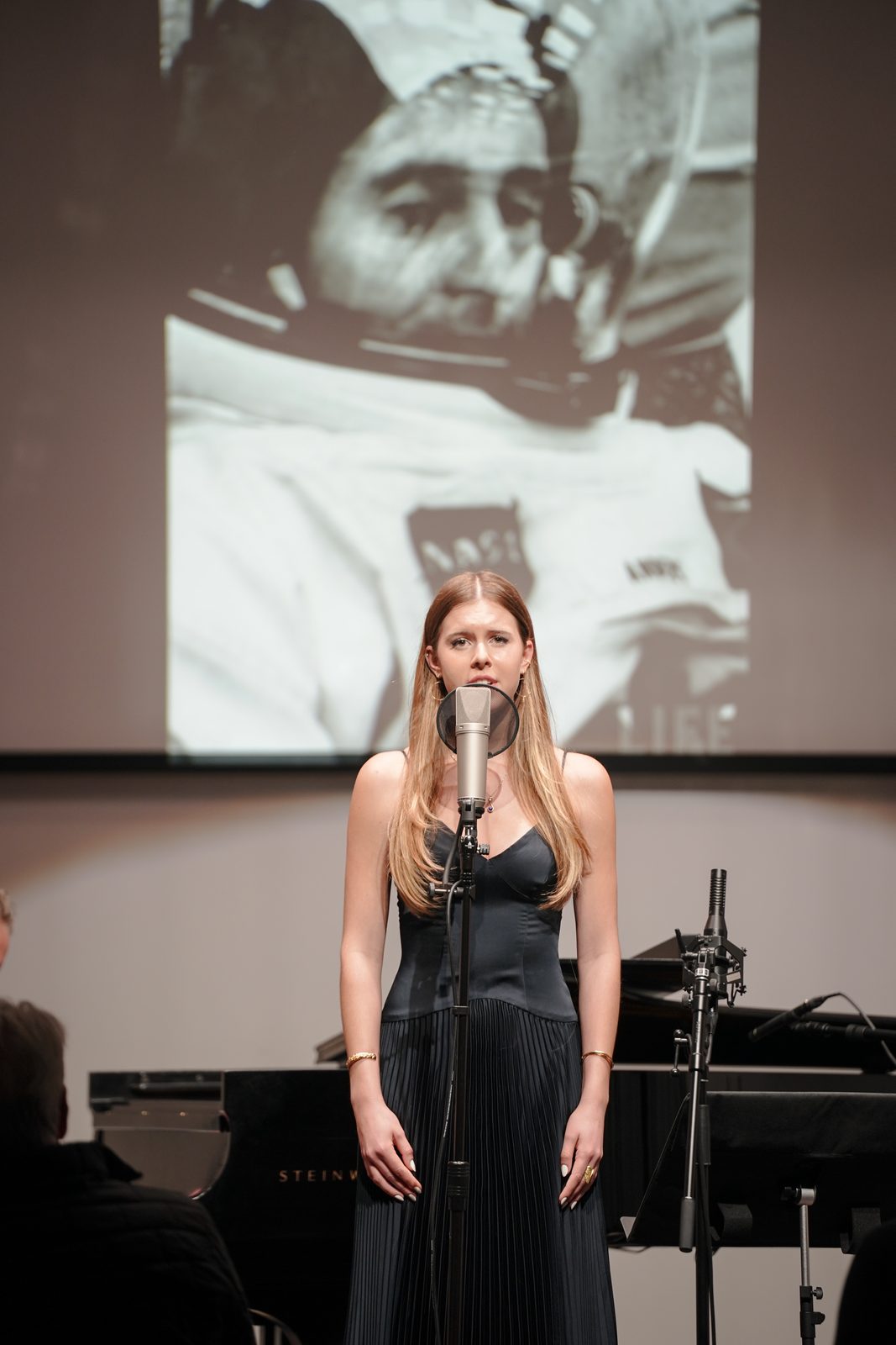 Lilah Anders sings beneath a photograph of her grandfather, Apollo 8 astronaut Bill Anders, in his spacesuit